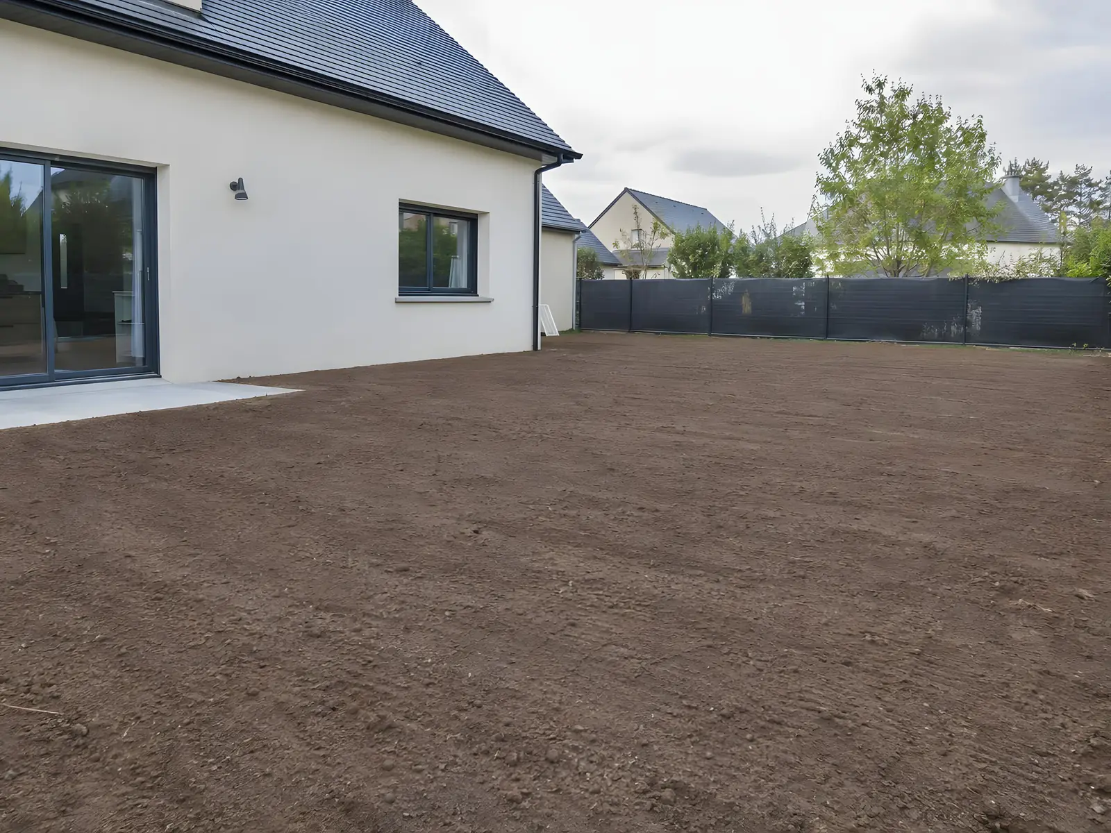 Le même jardin débarrassé de ses ronces et de ses souches, terre brune nivelée jusqu'à la clôture
